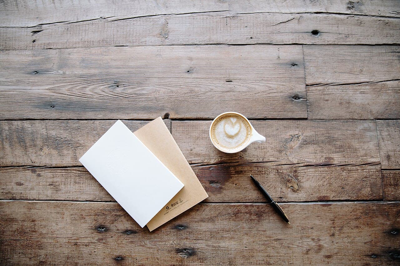 Notebooks, a pen and coffee on a wooden table